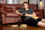 Mapa de la obesidad en España: un tercio de los niños tiene sobrepeso NIño obeso comiendo 'fast food' en el sofá de su casa y jugando a la videoconsola