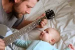 Los bebés perciben el ritmo de la música Padre toca la guitarra para su bebé en la cama