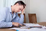 Hombre cabizbajo y deprimido haciendo las cuentas mensuales