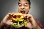Los antojos que nos hacen preferir alimentos ricos en grasas y azúcares se podrían explicar por los circuitos de recompensa que activan en el cerebro. Un hombre dándole un mordisco a una hamburguesa con deseo