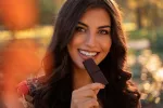 Comer chocolate negro puede ayudar a reducir el riesgo de hipertensión Mujer joven comiendo una tableta de chocolate negro