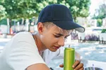 Los adolescentes que toman bebidas energéticas consumen más drogas Joven bebiendo una bebida energética sentado en un banco del parque