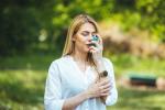 Mujer afectada por asma alérgica usando un inhalador en un parque
