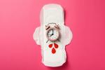 Un reloj somre una compresa simbolizando el tiempo para la próxima mestruación