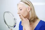 Vinculan la infección por herpes simple a un mayor riesgo de alzhéimer Mujer mayor observando con un espejo una herida que le ha salido en el labio