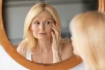 Revelan por qué algunas mujeres mayores están perdiendo sus cromosomas X Una mujer mayor observando como cambia su rostro en el espejo