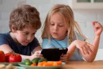 Reducir el tiempo de pantallas en familia mejora la salud mental de los niños Hermanos pequeños jugando co el móvil en la cocina