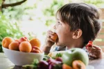 Expertos recomiendan cómo cuidar la alimentación de los niños en verano Niño comiendo fruta al aire libre