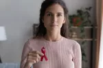Generaciones posteriores a Baby boomers tienen más riesgo de cáncer Mujer joven sostiene lazo rosa símbolo de cáncer de mama