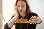 Alopecia posparto: causas, soluciones y cuándo preocuparse Mujer mirando asombrada el cepillo del pelo lleno de cabello