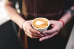 Asocian el café y la cafeína con menor riesgo cardiometabólico Hombre sostiene una taza de café con un corazón dibujado en la espuma