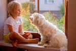 Los niños que conviven con perros tienen mejor salud intestinal Niño pequeño habla a su perro sentado junto a él