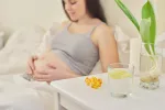 Suplementos de vitamina D en el embarazo mejoran la salud ósea del bebé Mujer embarazada tumbada en la cama junto a unas píldoras de vitamina d