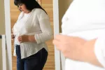 La grasa visceral se asocia con el desarrollo de alzhéimer Mujer con obesidad abdominal se viste frente a un espejo