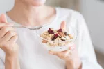 Dieta rica en fibra ayudaría a retrasar el mieloma Mujer toma un bol de cereales y yogur rico en fibra
