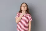 Ciertas enfermedades pueden contribuir al desarrollo de disfagia en niños Una niña con disfagia se toca la garganta con gesto de dolor