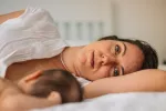 Test ¿Sufres depresión posparto? Mujer tumbada en la cama con la mirada perdida junto a su bebé recién nacido