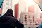 Desigualdades socioeconómicas afectan negativamente a la salud mental Hombre pobre mira edificios de viviendas desde su tienda de campaña