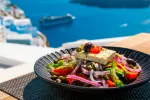Descubren el secreto de la dieta mediterránea para potenciar la memoria Plato de ensalada griega sobre un paisaje de mar