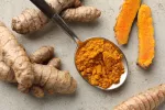 La curcumina puede mitigar daño cerebral causado por crisis epilépticas Cuchara con curcumina en polvo rodeada de plantas de cúrcuma