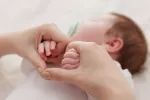 Aumentan los nacimientos en España por primera vez en la última década Manos de mujer sujentan las manitas de un bebé dormido