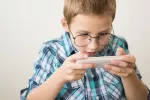 Un mayor uso diario de pantallas se asocia a un aumento de la miopía en niños y jóvenes Niño con gafas mira fijamente una consola mientras juega