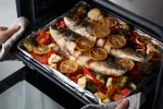 Consumo de pescado blanco y azul reduce discapacidad en pacientes con esclerosis múltiple Mujer saca una bandeja del horno con pescados y verduras