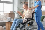 Estiman un significativo aumento de los casos de párkinson para 2050 Hombre con párkinson en silla de ruedas junto a una enfermera en su casa