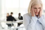 Experimentar más síntomas en la menopausia puede aumentar el riesgo de demencia Mujer madura en la oficina se toca las sienes con gesto de sentirse mal