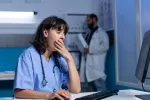 Trabajar de noche aumenta el riesgo de infecciones en las enfermeras Enfermera bosteza frente al ordenador durante un turno de noche