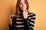 Tomar una o más bebidas azucaradas al día puede aumentar el riesgo de cáncer oral en mujeres Mujer joven sostiene un refresco y duda si tomarlo