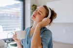 Una joven escucha música con auriculares mientras toma un café en su cocina