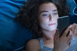 Usar dispositivos digitales en la cama antes de dormir afecta a la calidad y duración del sueño Mujer joven mirando su móvil en la cama por la noche
