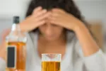 El consumo de 8 bebidas alcohólicas por semana puede deteriorar la memoria Mujer con las manos sobre la frente y actitud pesarosa junto a una botella y un vaso de wisky