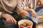 Una alta ingesta de pollo y otras aves de corral puede aumentar el riesgo de cáncer gastrointestinal Dos personas comen pollo frito comprado en una cadena de comida rápida