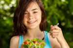 Una alimentación saludable en la infancia puede retrasar la primera regla de las niñas Una niña sonríe mientras se dispone a comerse una ensalada
