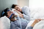 Hombre con mascarilla nasal CPAP para tratar la apnea del sueño Hombre joven con dispositivo CPAP duerme junto a su pareja