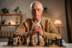 Hombre mayor pensativo delante de un tablero de ajedrez