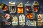 Latas de conservas de pescados abiertas, ¿saludables? Diversas latas de conservas de pescados abiertas sobre una tabla de pizarra