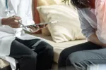 Mujer con dolor abdominal consulta a su médico Mujer joven con molestias abdominales junto a su médico que consulta unos datos