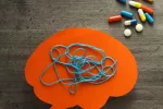 Medicamentos para tratar la esquizofrenia junto a un cerebro de papel con hilo enredado Cerebro de papel con hilo enredado junto a diversos medicamentos