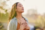 Una mujer practica ejercicios de respiración al aire libre Mujer joven inspira con los ojos cerrados y las manos sobre el pecho
