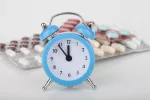 Hora a la que tomar la medicación Reloj azul marca casi las 12 y detrás varios blíster de medicamentos
