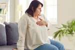 Mujer con sobrepeso con síntomas de infarto de miocardio Mujer obesa sentada en su casa se toca el pecho con gesto de dolor