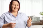 Mujer obesa sonríe sosteniendo una píldora y un vaso de agua