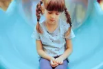 Niña triste y sin ganas de jugar sentada en el patio de recreo Niña pequeña sentada con expresión triste