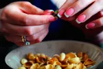 Beneficios del consumo de pistachos para la salud Manos de mujer con uñas pintadas pelan pistachos