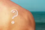Protector solar: dudas de cuándo usarlo Interrogante hecho con protector solar en la espalda de un hombre en la playa