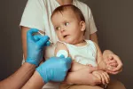 14 millones de bebés sin vacunas Cuidador sostiene a un niño pequeño en preparación para una vacunación