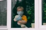 Niño con síndrome post-COVID grave MIS-C Niño con mascarilla y un peluche con mascarilla mirando tras una ventana
